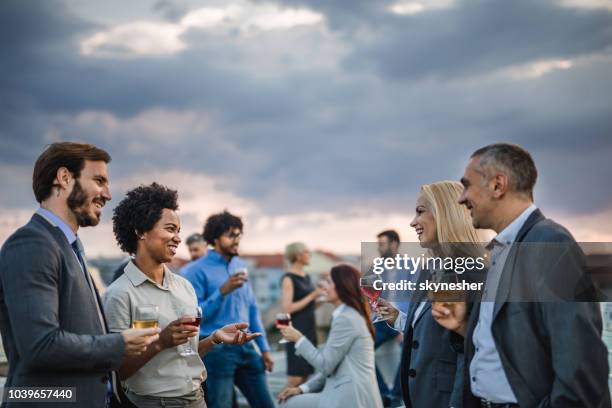 happy business people talking while drinking alcohol on a rooftop party. - rooftop deck stock pictures, royalty-free photos & images