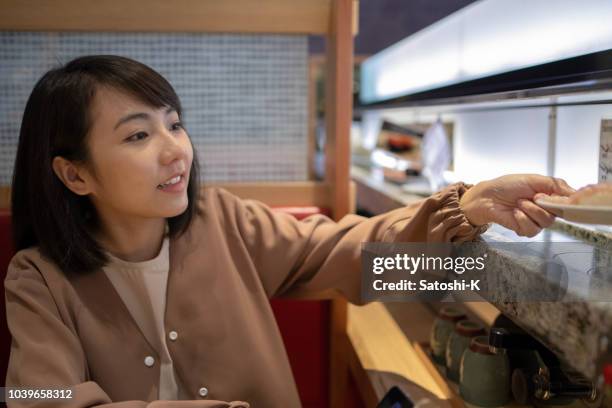 asian tourist trying sushi at restaurant - sushi train stock pictures, royalty-free photos & images