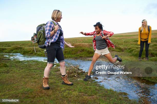 hiking friends jump over a small stream in the countryside. - dougal waters 個照片及圖片檔