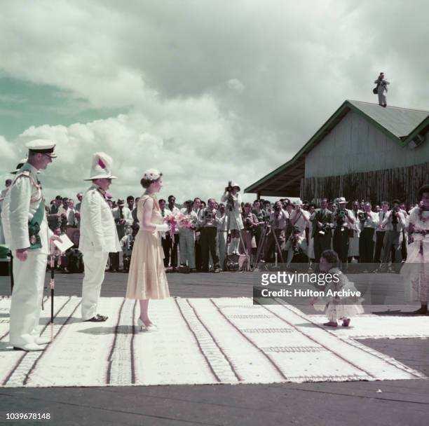Queen Elizabeth II is greeted by a young girl at an official welcome at a quayside in Fiji during the coronation world tour, December 1953. Behind...