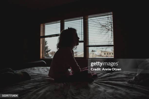 silhouette of little girl sitting on bed - dark background light stock-fotos und bilder