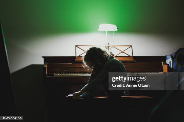 girl on a piano bench lit by a piano light behind her - curls girl silhouette ストックフォトと画像