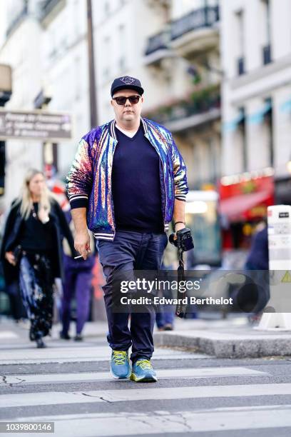 Guest wears a cap, a shiny jacket, blue sneakers with green shoelaces, outside Gucci, during Paris Fashion Week Womenswear Spring/Summer 2019, on...