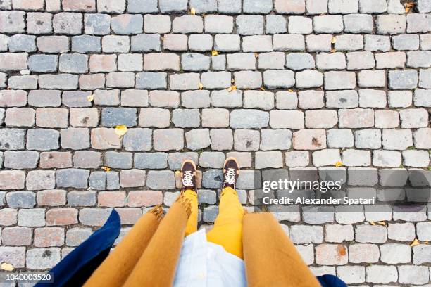 personal perspective of low section of a man in sneakers and yellow trousers at cobblestone street - cobblestone texture stock pictures, royalty-free photos & images