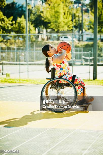 Young female adaptive athlete preparing to shoot basketball on outdoor court on summer evening