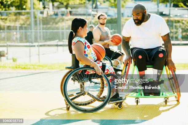 smiling young female adaptive athlete getting advice from adaptive basketball coach during practice on summer evening - child in wheelchair stock-fotos und bilder