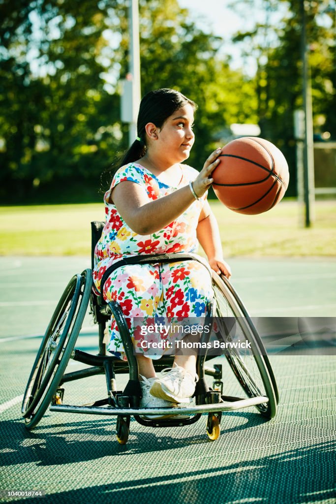 Young female adaptive athlete dribbling basketball on outdoor court on summer evening