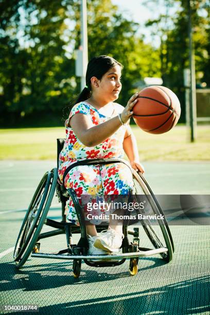 Young female adaptive athlete dribbling basketball on outdoor court on summer evening