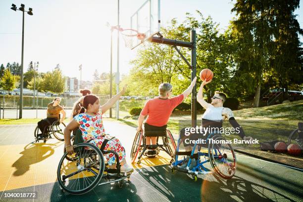 adaptive athlete playing pickup wheelchair basketball on outdoor court on summer evening - summer super 8 stockfoto's en -beelden