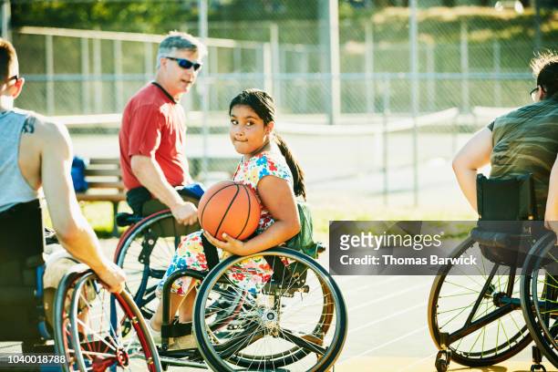 Young female adaptive athlete playing wheelchair basketball on summer evening