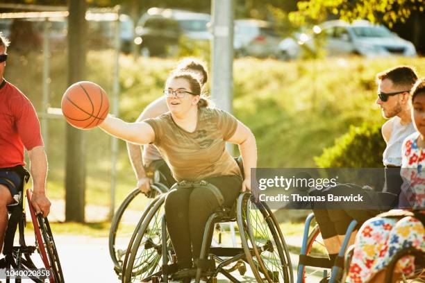adaptive female athlete stretching for ball during wheelchair basketball game on summer evening - wheelchair basketball stock pictures, royalty-free photos & images