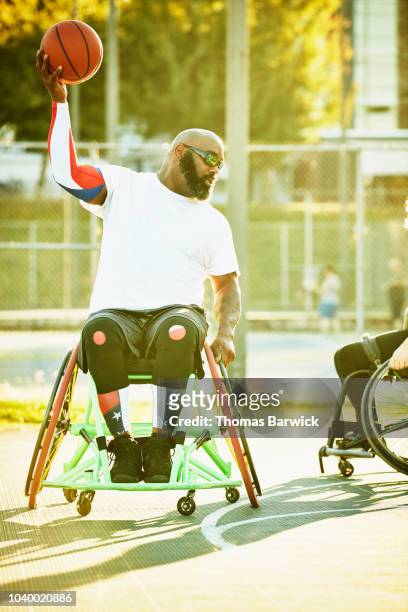 Adaptive athlete preparing to pass ball during wheelchair basketball game on summer evening