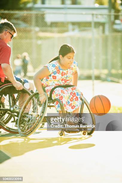 Young female adaptive athlete racing for ball during wheelchair basketball practice