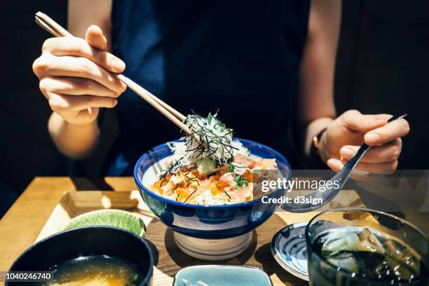 close up of woman enjoying freshly served traditional japanese seafood donburi with chopsticks in a restaurant - アジア料理 ストックフォトと画像