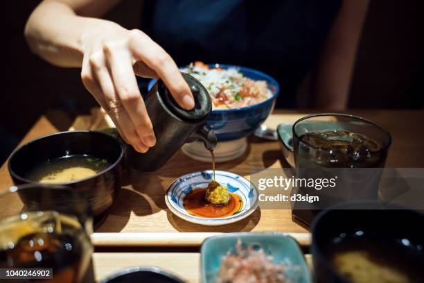 woman's hand pouring soy sauce over plate and ready to enjoy the fresh japanese seafood rice bowl in restaurant - soy sauce stock pictures, royalty-free photos & images
