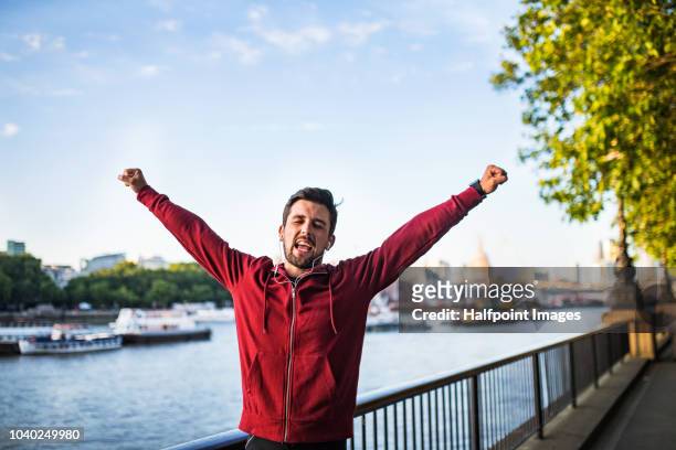 young sporty man with earphones standing on promenade outside in a london city, listening to music. - england slovakia stock pictures, royalty-free photos & images