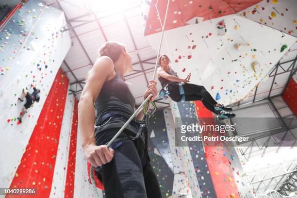 two young women on an indoor climbing wall. - woman climbing rope stock-fotos und bilder