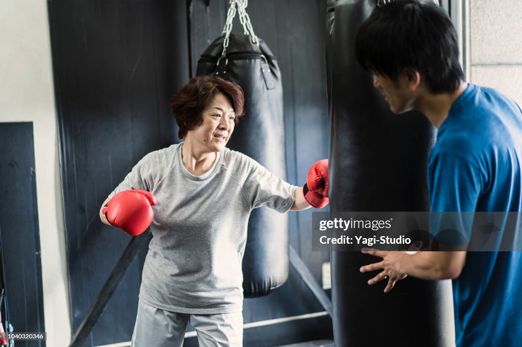 Senior adult woman training at boxing gym with coach