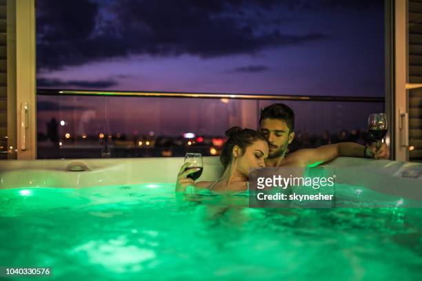 jovem casal relaxando na banheira de água quente na sua cobertura à noite. - couple bathtub - fotografias e filmes do acervo