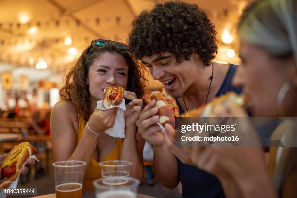 multiracial happy young people laughing and eating together at carnival - processed meat stock pictures, royalty-free photos & images