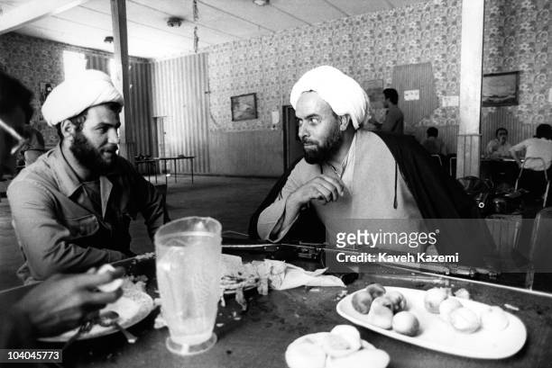 An Iranian cleric , armed with an AK-47 assault rifle, at lunch with a younger man after an Iranian counter offensive at Hajomran in northern Iraqi...