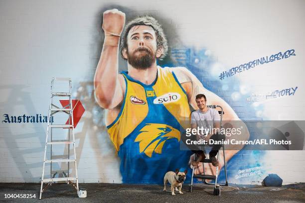 One of the two artists Jacob Butler poses with Banjo the French Bulldog in front his Josh Kennedy 2018 Mural commissioned by Seven West Media and the...