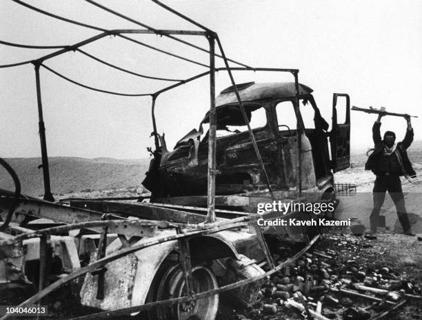An Iranian Revolutionary Guard holds his rifle aloft in triumph over a burned-out Iraqi truck, near Qasr-e Shirin, Iran, during the Iran-Iraq War,...