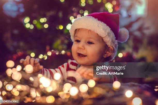 cute boy indoors near christmas tree - father christmas hat stock pictures, royalty-free photos & images