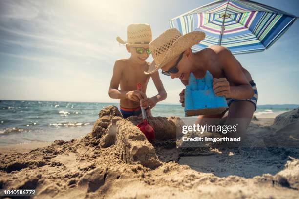 kleine jungs eine sandburg am strand bauen - beach umbrella sand stock-fotos und bilder