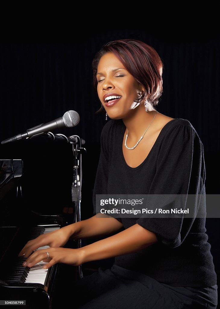 A Woman Playing The Piano And Singing Into A Microphone