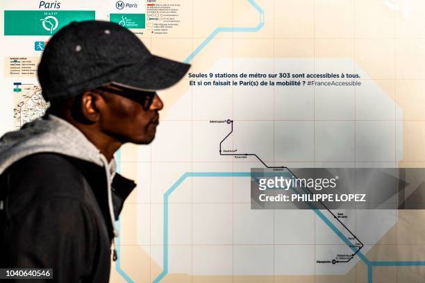 Man stands by a sticker covering a map of Paris' subway network showing that only 9 metro stations out of 303 are accessible to disabled and...