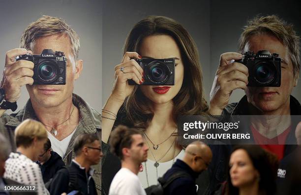 Fair goers walk past a poster advertising Lumix photo cameras on display at the Photokina trade fair for imaging on September 26, 2018 in Cologne,...