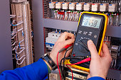 Multimeter in hands of electrician engineer in electrical cabinet. Maintenance of electric system. Worker tests of electrical circuit. Electrician with tester in hands.