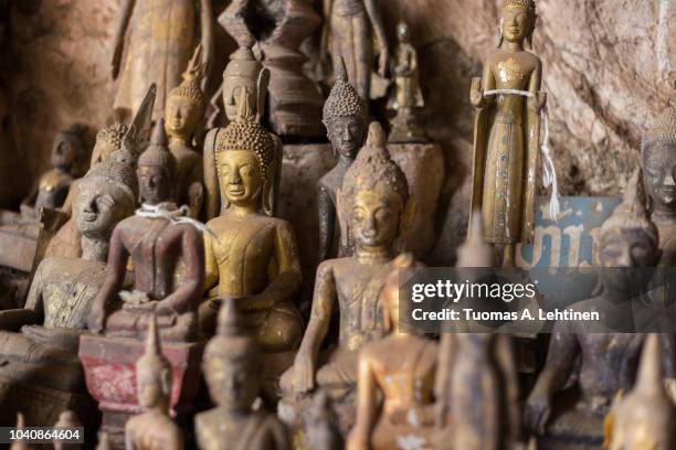 close-up of many old and faded, golden and wooden buddha statues inside the tham ting cave at the famous pak ou caves near luang prabang in laos. - pak ou caves stock pictures, royalty-free photos & images