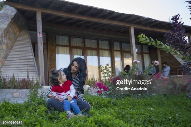 Woman and a little girl stare at each other on the front garden of a house, built with the inspiration from Hobbit houses in the movie "Lord Of The...