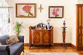 Real photo of an antique cabinet with porcelain decorations, paintings with roses and blue sofa in a living room interior