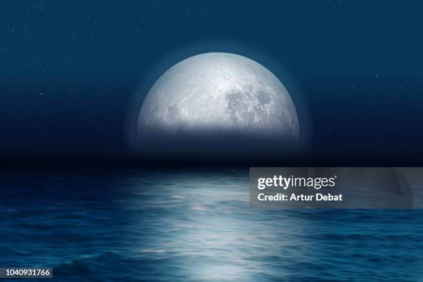 blue moon rising at night over the sea. - moon horizon stock-fotos und bilder