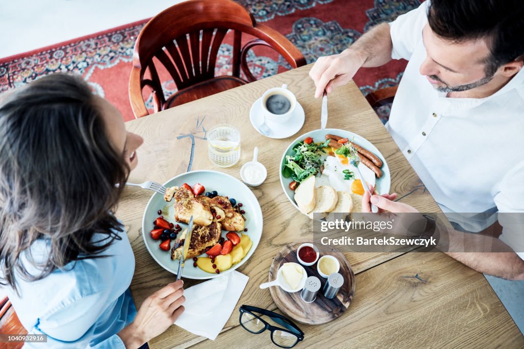 Cheerful couple having breakfast in cafe and talking. People eating together