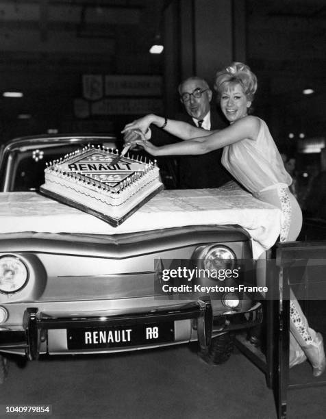 Une jeune femme et un homme âgé coupent un gâteau sur le capot du dernier modèle de véhicule Renault au Salon de l'Automobile à Earl's Court le 16...