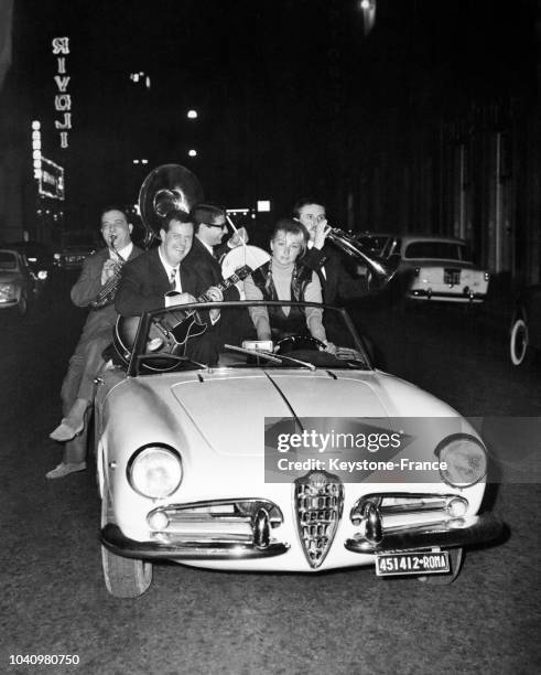 Actrice italienne Annie Gorassini à bord d'une voiture, entourée d'un orchestre de jazz dans les rues de Rome, Italie, en juin 1961.
