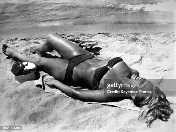 Une femme en maillot de bain prend un bain de soleil sur le sable au bord de l'eau en France, en 1962.