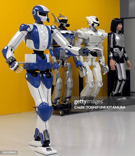 The HRP-4, a "slim athlete" robot, walks beside its previous models, the HRP-2 , the HRP-3 and the HRP-4C during a joint press preview by Kawada...