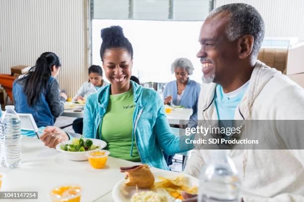 soup kitchen volunteers laugh together during a meal - homeless shelter man stock pictures, royalty-free photos & images