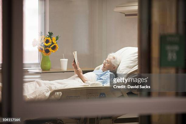 senior woman reading while lying in hospital bed - patient in bed stockfoto's en -beelden