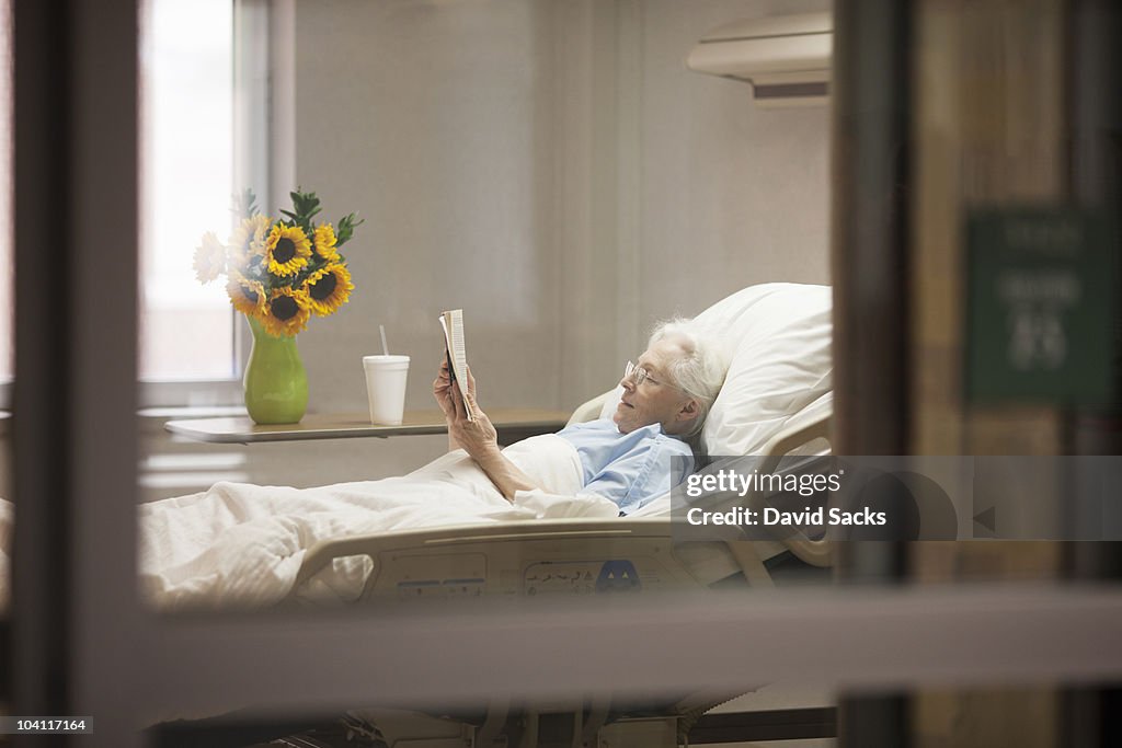 Senior woman reading while lying in hospital bed