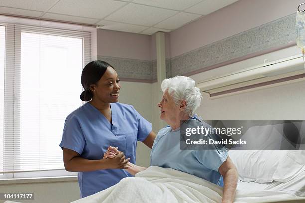 nurse helping 70s woman sit up in hospital bed - infirmière photos et images de collection