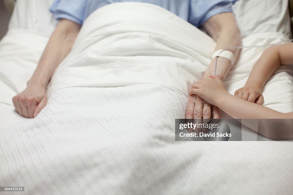 Young girl holding grandma's hand in hospital