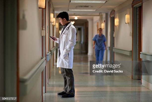 asian doctor in hospital corridor with phone - doctor smartphone stock pictures, royalty-free photos & images