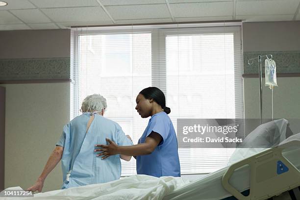 aa woman nurse helping patient stand up - old bed stockfoto's en -beelden