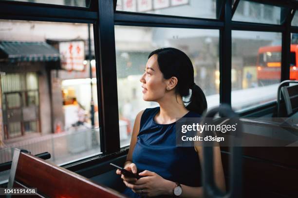 beautiful young asian lady with smartphone enjoying city scene through window while riding on public transportation in city - tourist china stock pictures, royalty-free photos & images